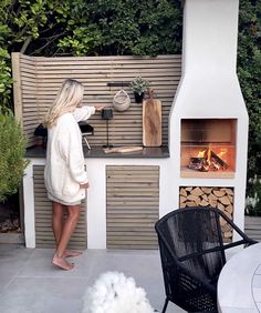 a woman standing in front of an outdoor pizza oven with wood logs and firewood