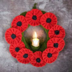 a knitted wreath with a lit candle in the center and red flowers on it