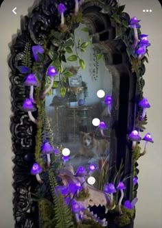 a mirror with purple flowers and green plants on the front is surrounded by white lights