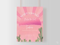 a pink poster hanging on a wall with cactus and sunburst in the background