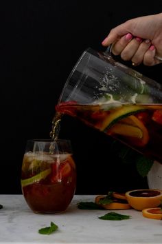 a person pouring liquid into a pitcher filled with fruit