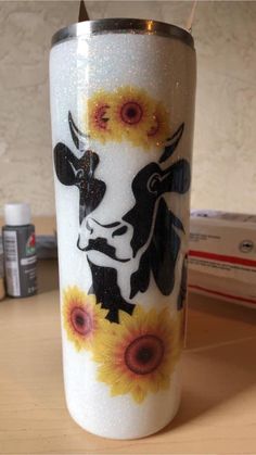 a white and black cow with sunflowers painted on it's side next to some other items