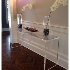 two clear vases with flowers in them sitting on a glass table next to a wall