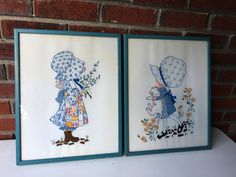 two framed pictures with children's artwork hanging on a brick wall next to each other