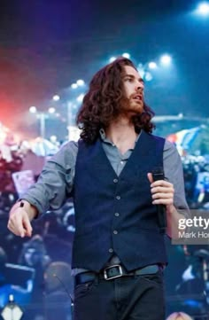 a man with long hair standing on stage holding a microphone in front of an audience