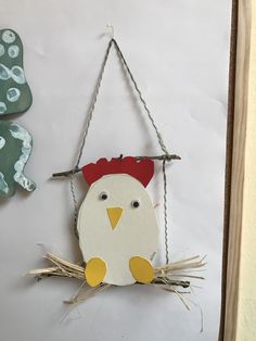 a chicken hanging from a string on the wall next to another bird that is wearing a red hat