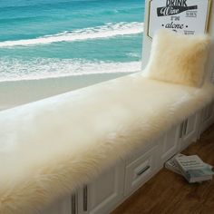 a white bench sitting on top of a hard wood floor next to the ocean and beach