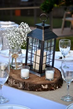 a candle is lit on top of a wooden table with white flowers and glassware