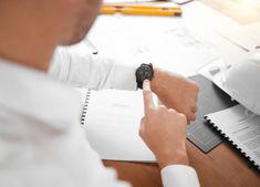 a man is pointing at the watch on his wrist as he sits at a desk