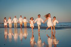 a group of people running on the beach in white clothes and tan pants, all holding hands with each other