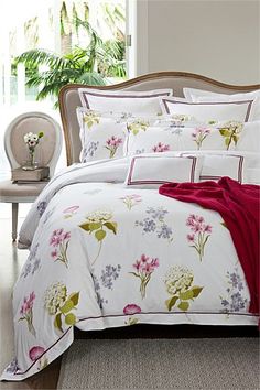 a bed with white and pink flowers on the comforter is in front of a window