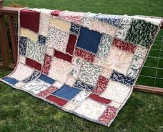 a patchwork quilt sitting on top of a wooden bench in the grass next to a fence