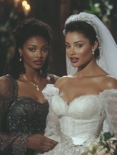 two women in wedding gowns standing next to each other and one is wearing a veil