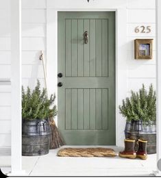 a green door and two buckets with plants on the front porch next to it