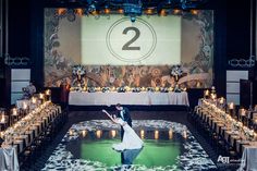 a bride and groom dancing on the dance floor in front of a large screen with candles