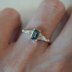 a woman's hand with a ring on it that has an emerald and white diamond