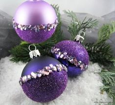 three purple christmas ornaments sitting on top of snow