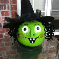 a green pumpkin with a witch hat on it's head sitting on top of a glass table