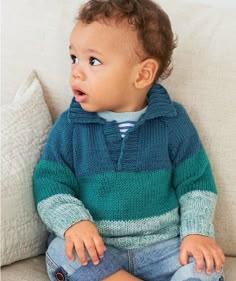 a small child sitting on top of a couch wearing a blue and green knitted sweater