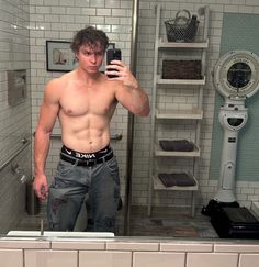 a shirtless man taking a selfie in the bathroom mirror with his cell phone