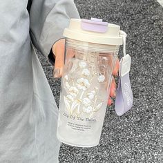 a person holding a plastic cup with flowers on it and a tag attached to the lid