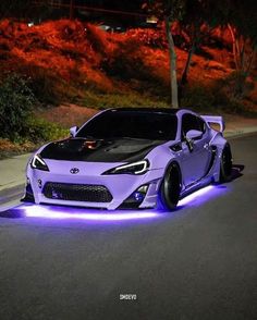 a purple sports car is parked on the side of the road with its lights on