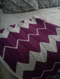 a crocheted blanket sitting on top of a bed next to a white pillow