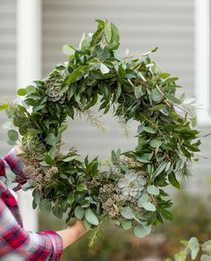 a person holding a wreath with greenery on it in front of a house,