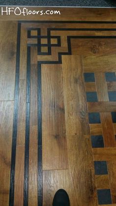 a wooden floor with black and white lines on it, next to a person's foot