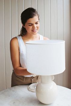 a woman sitting at a table with a white lamp on top of it and looking down