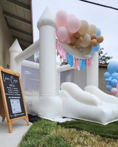 an inflatable slide and some balloons on the grass near a sign with a chalkboard