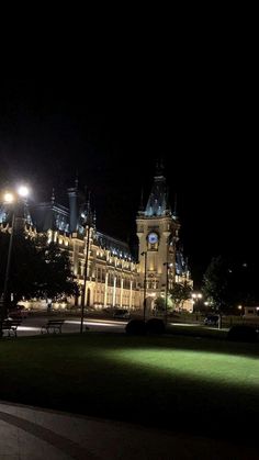 a large building lit up at night with lights on it's sides and grass in the foreground