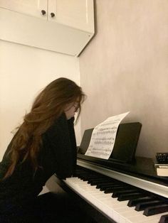 a woman sitting at a piano with sheet music on top of her head and long hair blowing in the wind