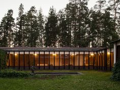 the house is surrounded by tall trees and has glass walls on each side that are lit up at night