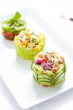 three small cucumbers on a white plate topped with lettuce and tomatoes