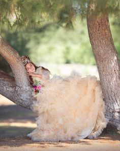 a woman in a wedding dress is sitting on a tree branch wearing a tiara