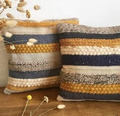 two decorative pillows sitting on top of a wooden table next to dried flowers and plants