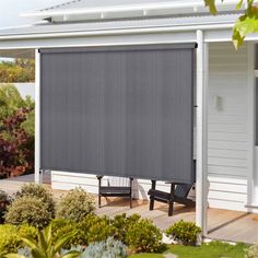 an outdoor patio area with a gray roller shade on the side of the house and two black chairs in front of it