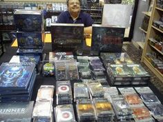 a man sitting behind a table full of dvds and games at a store in front of him