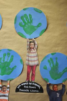 children holding up paper plates with handprints on them in front of a bulletin board