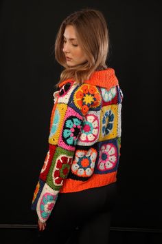 a woman wearing an orange and blue crochet sweater with colorful flowers on it