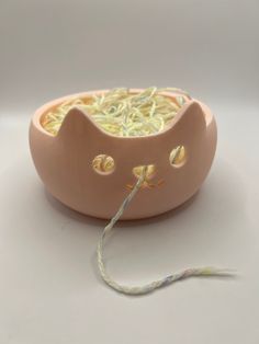 a cat shaped bowl with yarn in it's mouth and eyes on the side