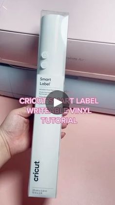 a person holding up a white tube in front of a pink box with the word cricut on it