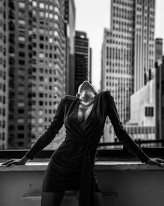 a woman standing on top of a balcony next to tall buildings in black and white