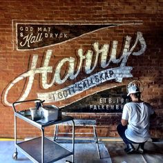 a man sitting on a stool in front of a brick wall with the words harry's painted on it