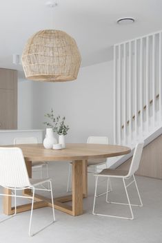 a wooden table with white chairs and a vase on top of it next to a stair case