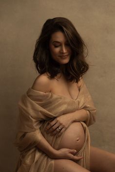 a pregnant woman poses for the camera in a gold dress with her hands on her belly