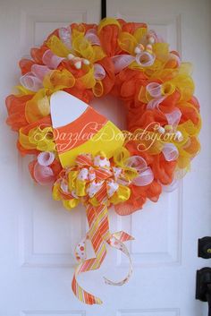 an orange and yellow wreath hanging on the front door with a candy cornucon