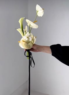 a hand holding a bouquet of flowers on top of a black stand in a white room