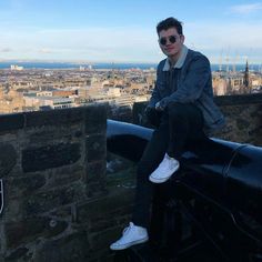 a man sitting on top of a stone wall next to a large cityscape